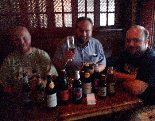 Tre menn på pub med masse ølflasker på bordet